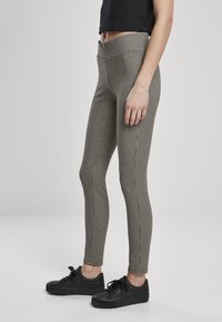 Fekete-fehér houndstooth mintás, textúrált anyagból készült, testhezálló leggings, rugalmas derékpánttal, fekete sportcipővel párosítva.