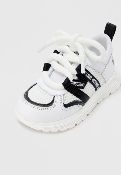 Λευκό αθλητικό παπούτσι με υλικά από δίχτυ και καουτσούκ, με μαύρες λεπτομέρειες, υπερμεγέθη λευκά κορδόνια και λουράκι με λογότυπο στο επάνω μέρος.