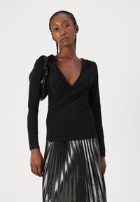 Maglietta nera a maniche lunghe con scollatura a V profonda e design avvolgente, abbinata a una gonna metallizzata plissettata. Tessuto liscio con una silhouette aderente.