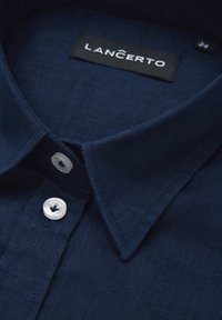 Granatowa lniana koszula z usztywnionym kołnierzykiem, białymi guzikami i metką markową. Tkanina ma gładką teksturę i subtelny blask. Widoczna metka z rozmiarem.