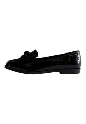 Zapato plano de charol negro con un detalle de lazo de tela suave en la parte delantera y un tacón bajo sobre un fondo blanco.