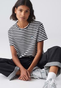 Zwart-witte gestreepte t-shirt met een ronde hals, zachte stof en een klein blauw hartdetail, gecombineerd met donker brede denim broek.