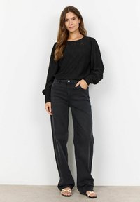 Black textured long-sleeve top with a diamond pattern, paired with high-waisted dark denim jeans and white sandals.