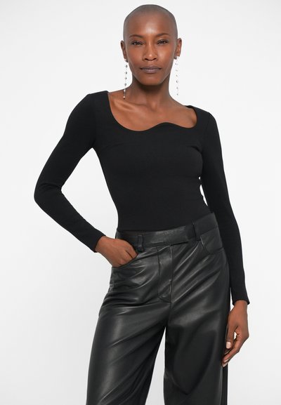 Top negro de manga larga con un diseño de cuello ondulado, combinado con pantalones de cuero negros de talle alto, que cuentan con una textura suave y un corte ajustado.