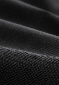 Gros plan d'un tissu noir texturé avec un motif fin tissé et des plis doux créant des contrastes de lumière et d'ombre.