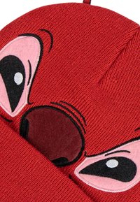 Berretto rosso lavorato a maglia con un design di personaggio caratterizzato da grandi occhi rosa e un prominente naso marrone. Texture morbida e forma superiore arrotondata.
