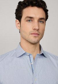Camisa de vestir a rayas azul claro con cuello abotonado, que presenta una tapeta en contraste con rayas azules y blancas en el interior.