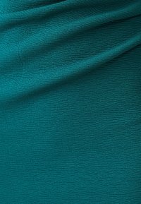 Tyrkysová látka s texturovaným povrchem, která má zvlněný vzor. Materiál vypadá měkce a mírně elasticky s jemným leskem.