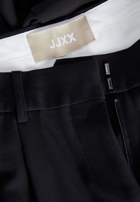 Svarta byxor med en slät tyg, midjeband med etikett, två metallaccenter och en diskret dragkedjestängning.