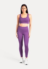 Paarse sport-bh en legging gemaakt van rekbare stof. Strak ontwerp met een gladde textuur en naadloze afwerking. Witte sneakers met accenten.