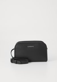 Borsa a tracolla in pelle nera con finitura testurizzata, bordi arrotondati, chiusura a zip e tracolla regolabile. Presenta un logo Lacoste in argento.