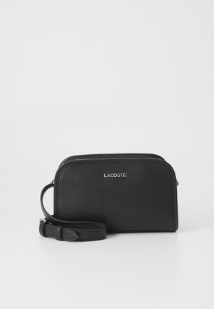 Melnas ādas pleca somiņa ar teksturētu apdari, noapaļotiem malas, ar rāvējslēdzēju un regulējamu siksnu. Izceļas ar sudraba Lacoste logo.