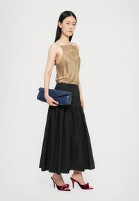 Beige satin cami top with lace trim, black pleated maxi skirt, blue textured clutch, and burgundy velvet heeled mules.