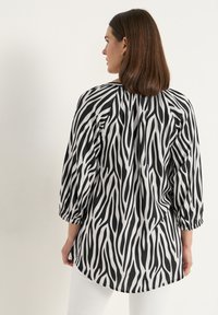 Zwart-witte blouse met zebraprint en driekwartmouwen. Lichtgewicht stof met een relaxte pasvorm, afgeronde zoom en details van een plooi aan de achterkant.