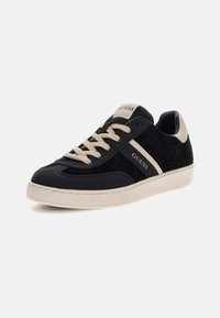 Schwarze und graue Sneaker aus glattem Leder und Wildleder, mit beigen Schnürsenkeln, einer weißen Gummisohle und dem "GUESS"-Logo an der Seite.