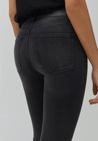 Mustat farkut, joissa on istuva malli, kaksi takataskua ja sileä kangaspinta, esitetty takaa päin.