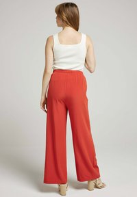 Haut blanc sans manches avec des bords festonnés, associé à un pantalon orange taille haute à jambes larges et des sandales à talons épais beiges.