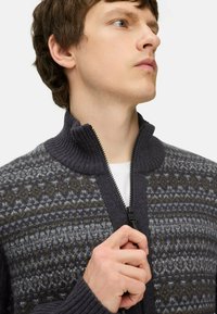 Grijze zip-up sweater met een geborduurd patroon in grijstinten en bruin, geribbelde kraag en ritssluitingen. Zachte textuur, tailormade pasvorm.