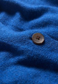 Blått tyg med en strukturerad väv, som har en brun knapp med fyra hål som är något förskjuten från mitten, vilket framhäver tygets djup.