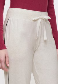 Crème-kleurige joggers met een zachte textuur, voorzien van een elastische tailleband, een trekkoord en zwarte zijkanten.