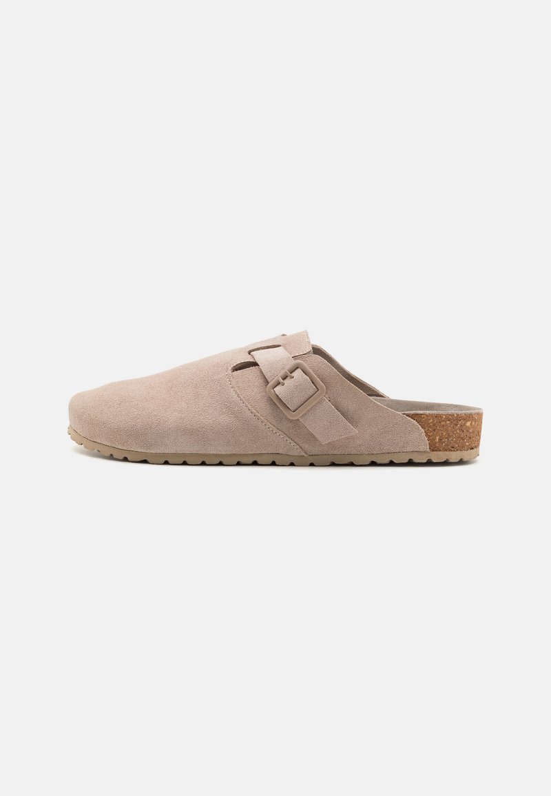 Beige semskede tresko med flad korksål, som har et sidespænde og rund tådesign, der tilbyder en glat tekstur.