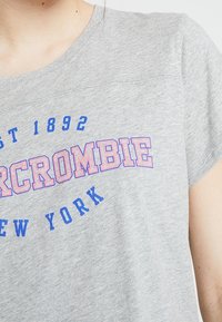 Graues Kurzarm-T-Shirt mit blauem und pinkem "Abercrombie"-Text und "New York" in einer gebogenen Schriftart aufgedruckt. Weiche Stofftextur.