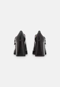 Black leather high-heeled shoes with a block heel, pointed toe, and a small bow detail at the back; smooth texture and sleek design.