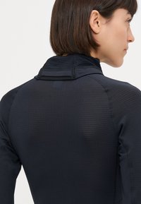 Top atletico nero con texture a coste, colletto alto e chiusura con zip sul retro. Le cuciture decorative migliorano la vestibilità e la funzionalità.