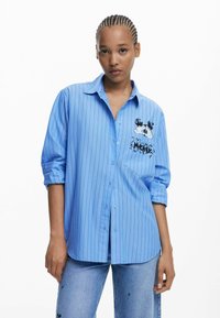 Lichtblauwe lange mouwen shirt met verticale strepen, voorzien van een zak met een zwarte Mickey Mouse graphic en knopen aan de voorkant.