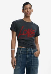 Schwarzes, kurzes T-Shirt mit einem großen roten "Love"-Grafik und Strassakzenten, kombiniert mit hochgeschnittenen blauen Jeans.