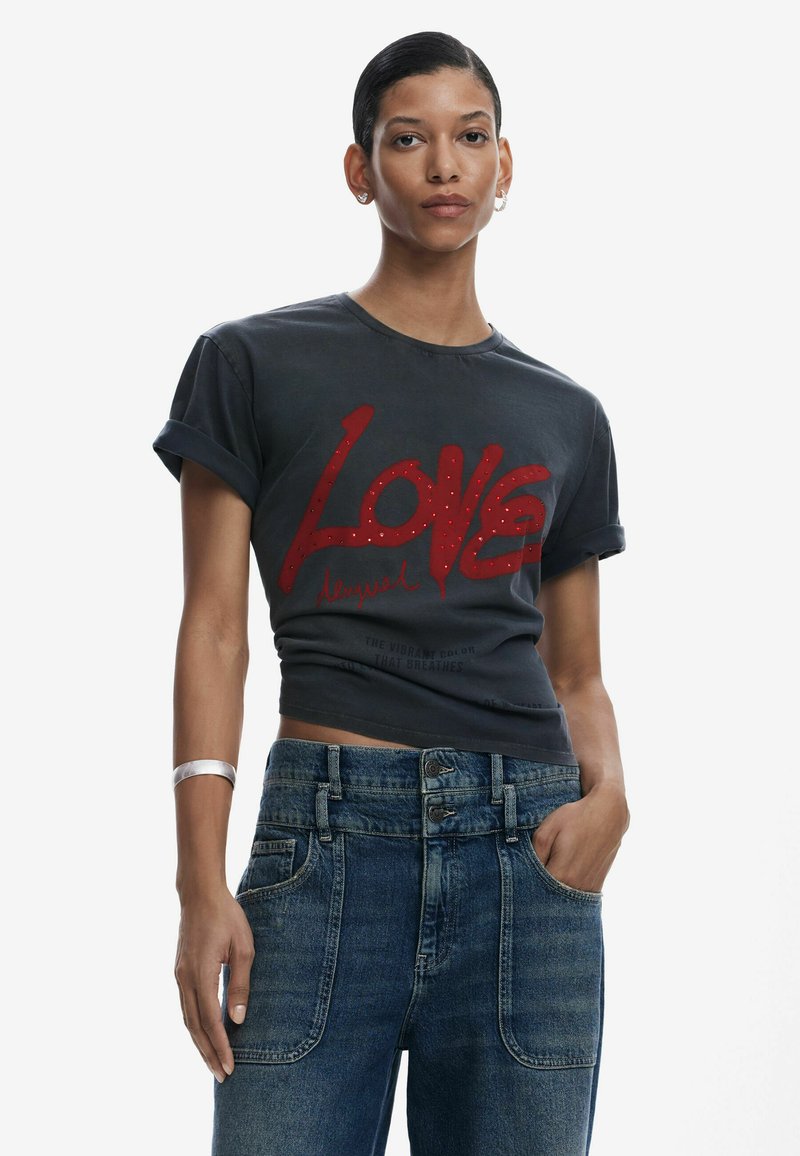Schwarzes, kurzes T-Shirt mit einem großen roten "Love"-Grafik und Strassakzenten, kombiniert mit hochgeschnittenen blauen Jeans.