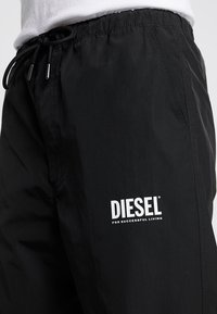 Black drawstring pants featuring a lightweight fabric, elastic waistband, and a prominent white "DIESEL" logo on the left thigh.