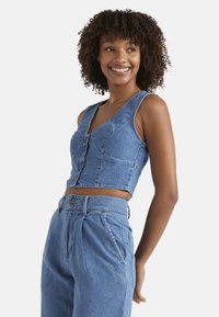 Dunkelblaues Crop-Top aus Denim mit Knopfleiste, V-Ausschnitt und ärmellosem Design. Hellblaue Farbe mit strukturierten Nähten und tailliertem Schnitt.