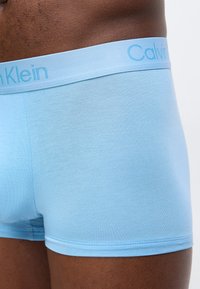 Κοντινό πλάνο ενός ατόμου που φοράει ανοιχτό μπλε ανδρικά εσώρουχα boxer Calvin Klein με ευδιάκριτο λογότυπο στην μέση.