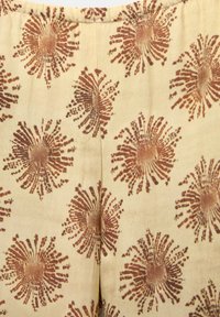 Beige stof met een herhaald patroon van grote, roestkleurige abstracte bloemontwerpen. Soepele textuur met een lichte glans.
