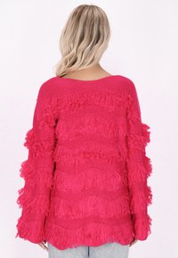 Roze gebreide trui met golvende franjes langs de mouwen en het lichaam, voorzien van een losse, wijde hals en textuurstof.