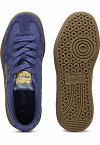 Puma sporta apavi violetā zamšā un ādā, ar apaļu gumijas zoli ar apļa rakstiem un mīkstu mēli. "Super" logotips dzeltenā krāsā.