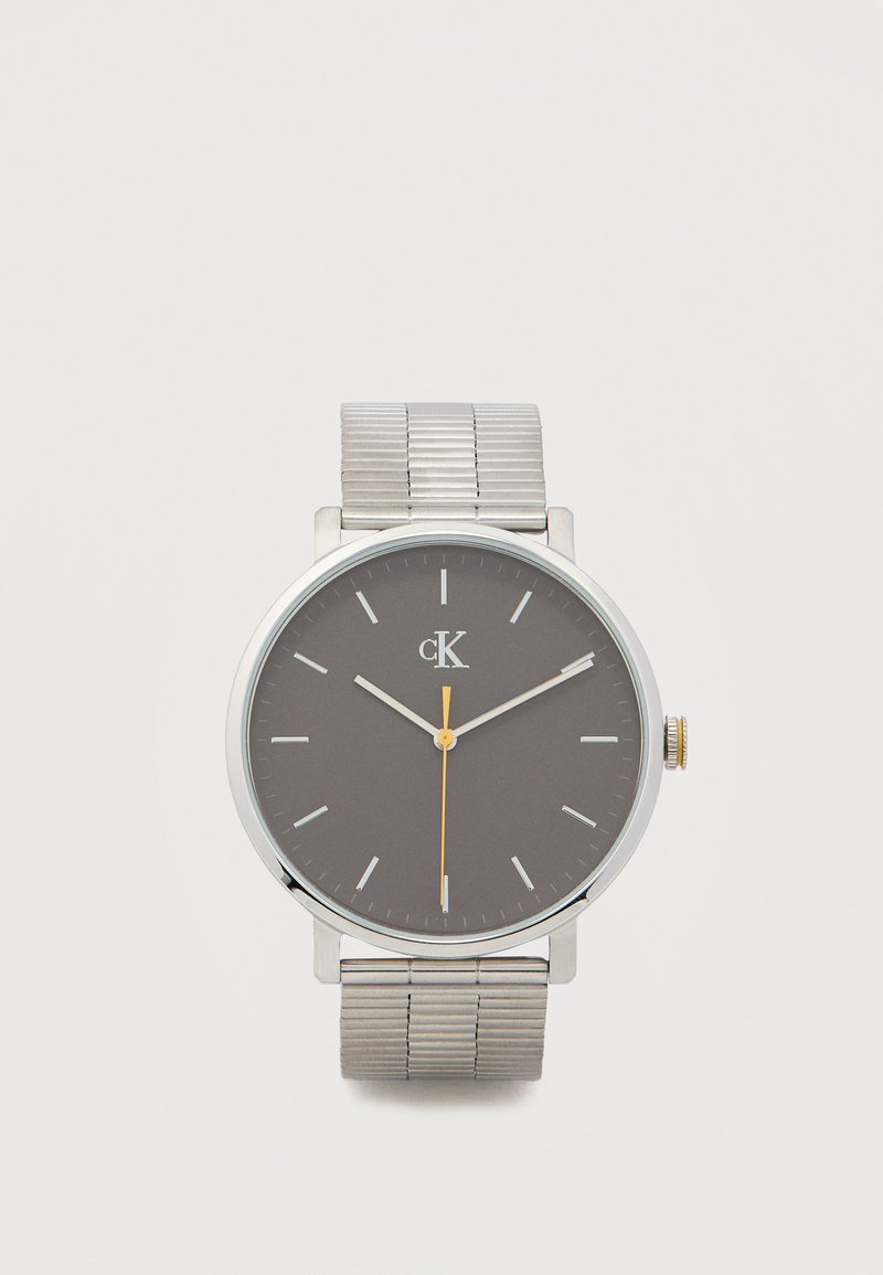 Montre-bracelet en argent avec cadran gris, marqueurs d'heure blancs minimalistes, aiguilles fines en argent, aiguille des secondes jaune, et bracelet métallique extensible.