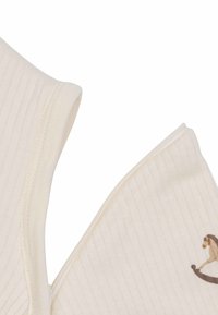 Tissu en coton, côtelé, de couleur crème avec une texture douce. Présente un petit design imprimé d'un animal brun sur un côté.