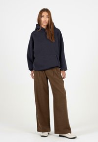 Marineblauwe pullover hoodie met een voork pocket, relaxed fit, gecombineerd met brede bruine broeken en witte schoenen, tegen een effen achtergrond.