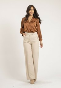 Blouse en satin marron avec un col en V et des manches longues, associée à un pantalon large beige taille haute. Bottines en suède neutre.