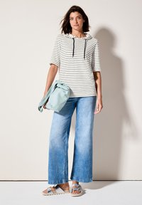 Randig huvtröja i vitt och svart, kombinerad med ljusblå vida jeans. Modellen håller en mintgrön väska och bär silverfärgade sandaler.