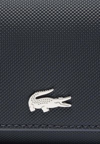 Material texturizado de un azul marino oscuro con un patrón en relieve; presenta un logo de cocodrilo plateado, que añade un detalle notable al diseño.