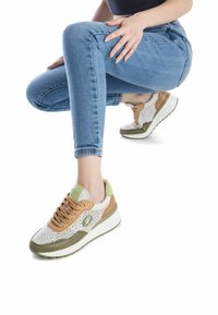 Zapatillas blancas y color canela con parte superior perforada, detalles en verde y suela de goma. Cuentan con cierre de cordones y collar acolchado para mayor comodidad.