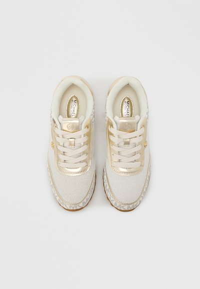 Λευκά αθλητικά παπούτσια με χρυσές λεπτομέρειες, διαθέτοντας επάνω μέρος από υφασμάτινο υλικό με υφή, κλείσιμο με κορδόνια και σόλα με σχέδιο. Το λογότυπο εμφανίζεται στη γλώσσα.