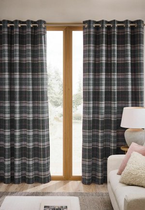 Dark plaid curtains hang on a wooden framed glass door with a white lamp and pillows on a beige sofa nearby.