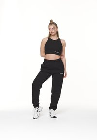 Svart crop topp med logo, parret med svarte joggebukser. Materialet ser mykt og teksturert ut. Fullført med hvite sportssko.
