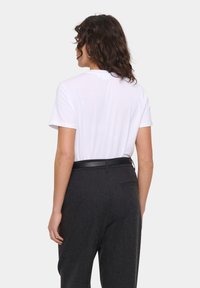 Tricou alb cu maneci scurte și guler rotund, asortat cu pantaloni gri închis, având o curea neagră subțire. Țesătura pare netedă și ușoară.