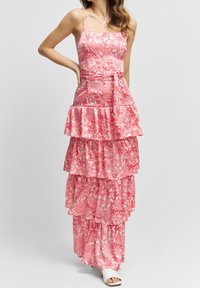 Robe maxi à imprimé floral rose avec des bretelles spaghetti, des volants à plusieurs niveaux et un détail de taille nouée. Fabriquée en tissu léger.