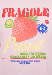 Ροζ ανοιχτό ρούχο με μεγάλο γράφημα ενός κόκκινου φράουλου, έντονα γράμματα σε διάφορα χρώματα και κυκλικά αυτοκόλλητα που περιγράφουν το προϊόν.